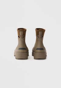 Botas de tobillo de caucho marrón con un acabado texturizado, elástico en los laterales y suela resistente. Presenta un logotipo en el talón y una parte superior de color contrastante.