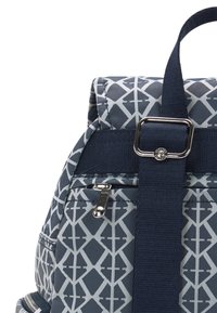 Navy sininen reppu, jossa on geometrinen valkoinen kuvio, varustettuna ylhäällä olevalla kahvalla, säädettävillä hartiohihnoilla ja vetoketjullisilla taskuilla, joissa on hopeiset yksityiskohdat.
