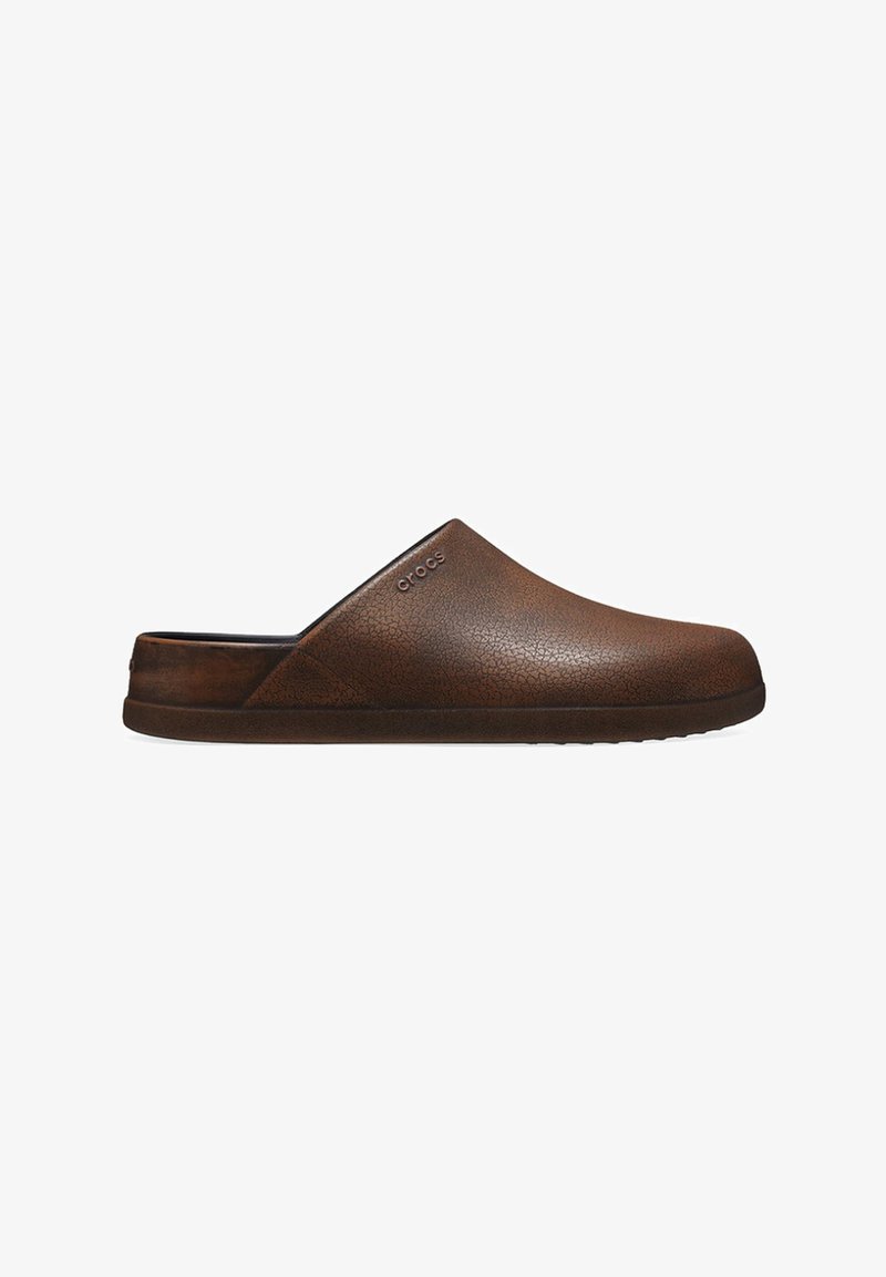 Calzature slip-on marroni con una parte superiore in materiale simile alla pelle, caratterizzate da una punta rotonda e una suola imbottita per il comfort. Logo sul lato.