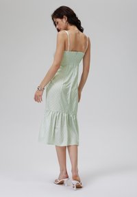 Robe midi vert menthe avec bretelles spaghetti réglables, corsage smocké, motif à pois et ourlet froncé. Portée avec des sandales à talons blanches.