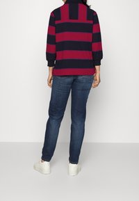 Flerfärgad randig topp med mörkblå och vinröda horisontella ränder, kombinerad med mörka jeans och vita sneakers.