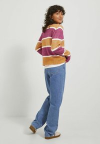 Wielokolorowy sweter w paski w odcieniach fioletu, pomarańczy i bieli, zestawiony z jasnoniebieskimi dżinsami. Miękka tekstura, luźny krój i okrągły dekolt.