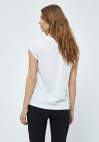 Camiseta blanca de manga corta con escote redondeado, que presenta un corte holgado y un material ligero. Combinada con pantalones negros.