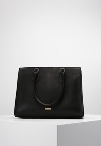 Czarna skórzana torba tote z dwiema okrągłymi uchwytami, prostokątny kształt, gładka tekstura i małe złote logo z przodu.