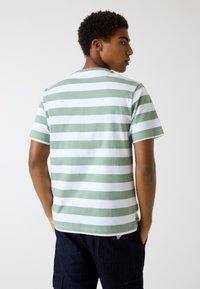 Grün-weißer gestreifter T-Shirt mit kurzen Ärmeln, Rundhalsausschnitt und lässiger Passform. Weicher Baumwollstoff mit glatter Textur.