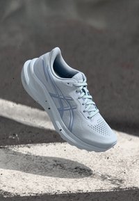 Scarpa sportiva azzurro chiaro con tomaia in rete traspirante, punta rinforzata e suola testurizzata che presenta piccole perforazioni e strisce decorative.