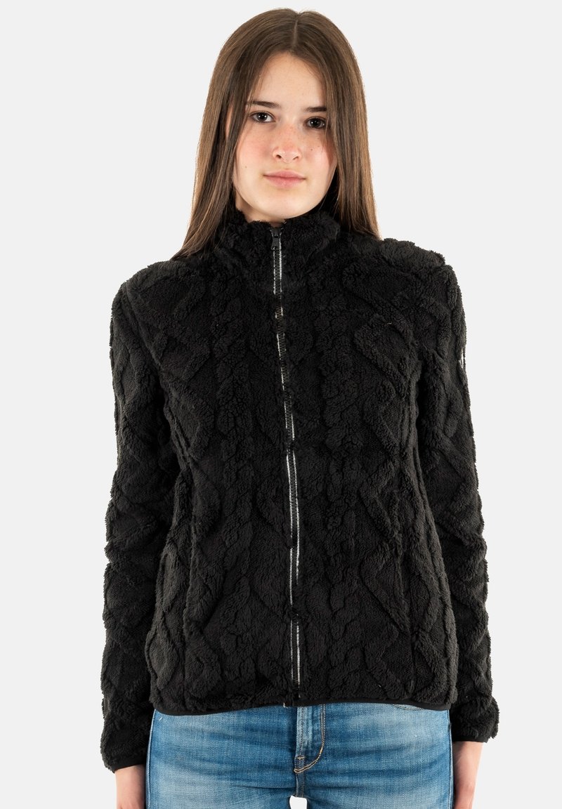 Chaqueta negra con cremallera, de tejido texturizado y suave, con un patrón geométrico y cuello alto, combinada con jeans azules. Apariencia suave y cálida.