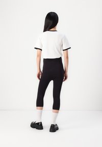Leggings negros de cintura alta combinados con una camiseta blanca de mangas cortas con ribetes negros. Se usan con zapatos negros gruesos y calcetines blancos.