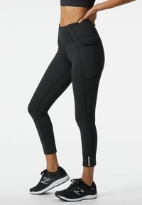 Leggings neri da allenamento con vita alta, caratterizzati da dettagli di cucitura discreti e un design aderente e slanciato. Abbinati a scarpe da ginnastica nere.