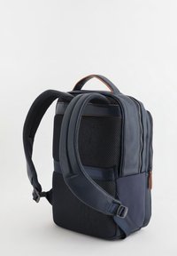 Mochila navy con paneles de malla, detalles de cuero y correas ajustables. Presenta un asa superior y compartimentos dobles con cremallera para almacenamiento.