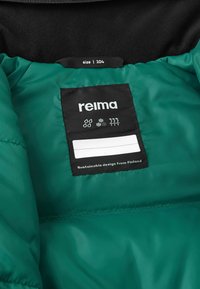 Groene geïsoleerde jas met een binnenkant en een zwart label. Label vermeldt maat 104 en duurzame ontwerp uit Finland. Gladde, glanzende textuur.