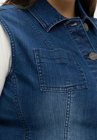 Jeansväst med en mörkblå tvätt, med knäppning fram, spetsig krage och en bröstficka med en rektangulär lock.