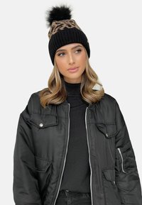Crna pletena kapa s uzorkom leopard printa i lažnim krznom na vrhu, nosi se s crnom bomber jaknom i turtleneck majicom. Glatka tekstura, topao dizajn.