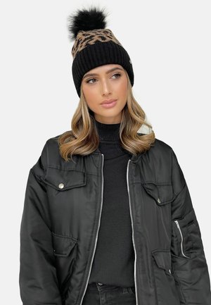 Zwart gebreid beanie met luipaardprint en een nep bont pompon, gedragen met een zwarte bomberjack en coltrui. Soepele textuur, warme uitstraling.