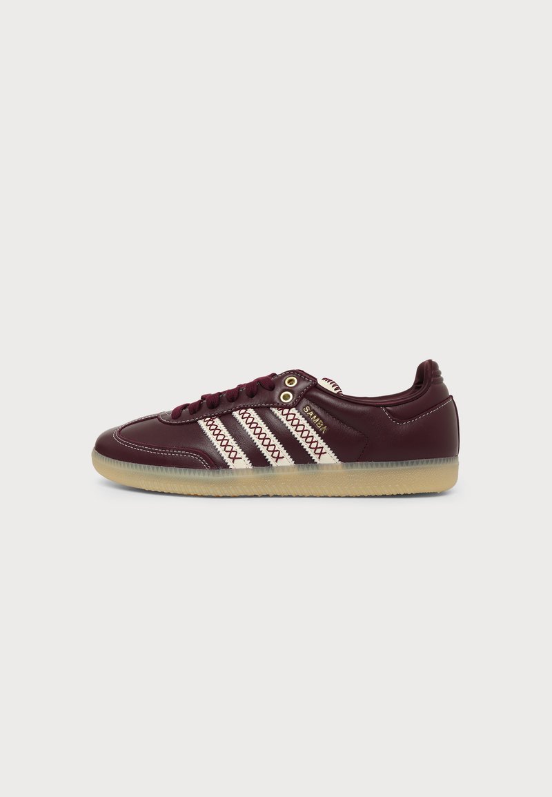 Κεραμιδί δερμάτινο sneaker Adidas Samba με λευκές ραμμένες ρίγες, καουτσούκ σόλα και χρυσό κείμενο "Samba" στη πλευρά, εμφανίζεται σε προφίλ.