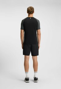 Svart kortärmad skjorta med grå raglanärmar, kombinerad med svarta shorts och svarta atletiska skor, sedd från baksidan.