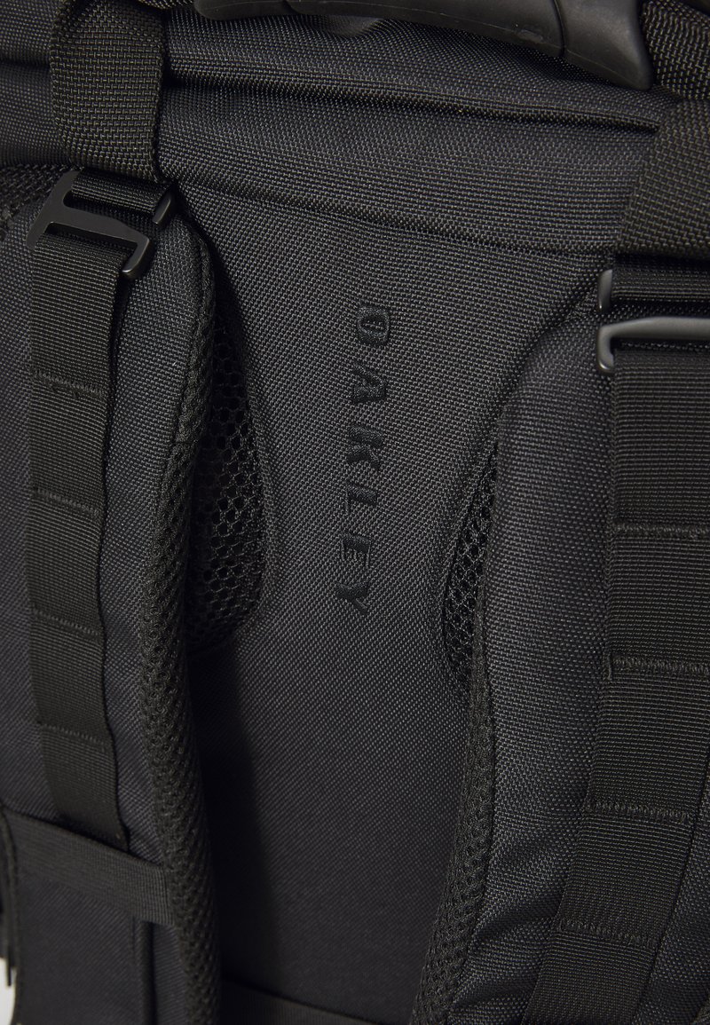 Sac à dos noir avec un tissu durable, des accents en maille, des bretelles réglables et un grand logo "OAKLEY" en relief.