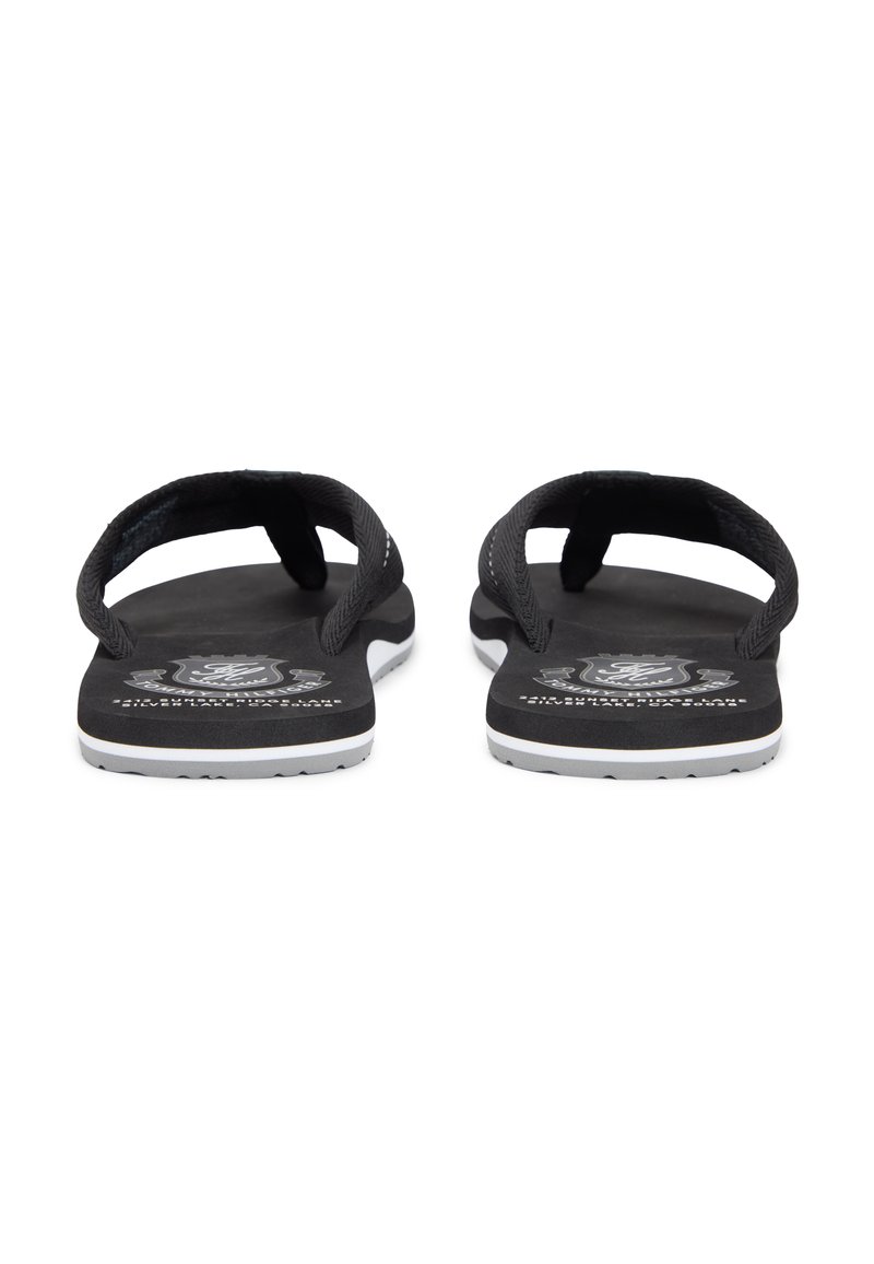 Chanclas negras con correas texturizadas, suela plana y detalles en blanco. Presentan un logo en la plantilla y un patrón de dibujo mínimo en la suela.