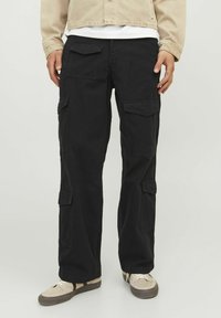 Pantaloni cargo negri cu multiple buzunare, croi lejer, dintr-un material cu o textură netedă. Purtați cu adidași bej.