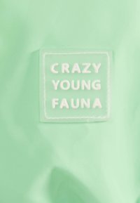 Mintgrön tyg med en glänsande yta, prytt med en rektangulär, präglad vit etikett som säger "CRAZY YOUNG FAUNA." Enkelt mönster och mjuk textur.