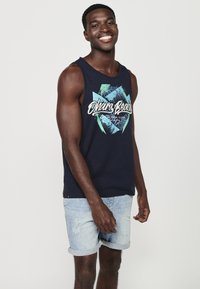 Tumedat sinise värvi sansihõlmadega t-särk, millel on "Ohana Beach" graafika, millel on rohelised ja valged aktsendid. Kandmiseks kergete denimshortsidega.