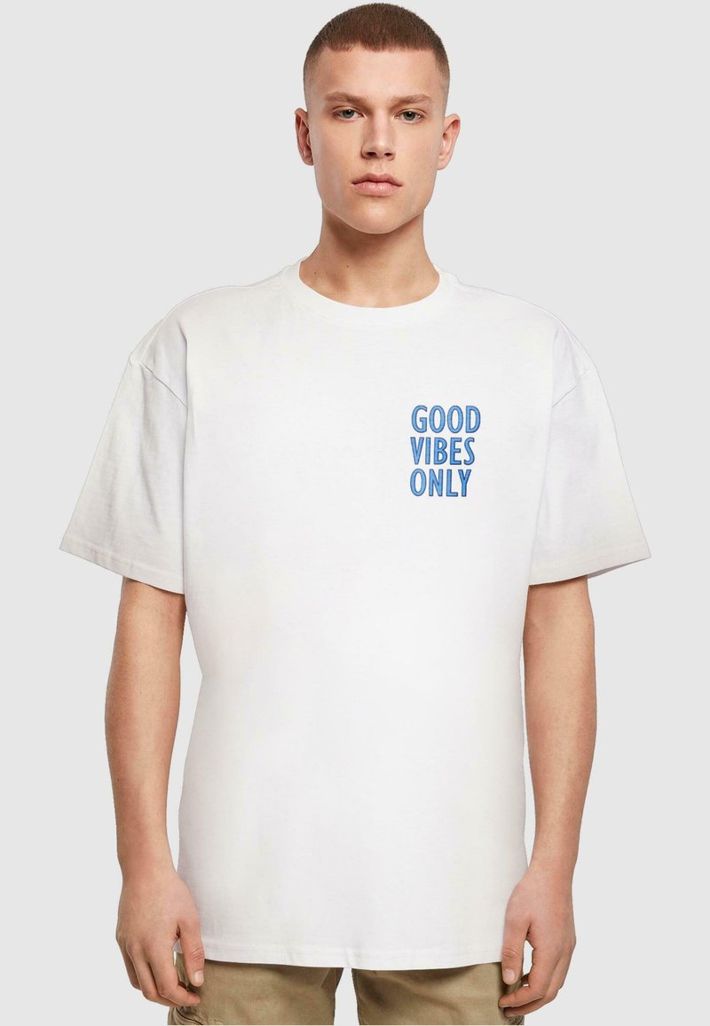 Hvid bomulds t-shirt med korte ærmer, der har blå trykt tekst "GOOD VIBES ONLY" på venstre brystområde. Klassisk crew neck design.