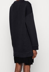 Svart oversized sweatshirt med långa ärmar, med rundad halsringning och sidslitsar, tillverkad av ett mjukt, texturerat tyg.