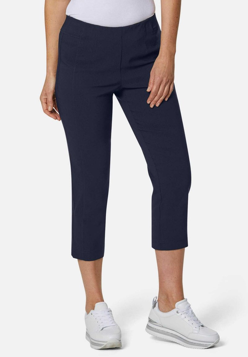 Marineblaue cropped Hose mit glatter Textur, elastischem Bund und Seitentaschen, kombiniert mit weißen Sneakers mit einem dezenten metallischen Akzent.