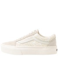 Niskie beżowo-białe trampki Vans z zamszowym czubkiem, tkaninowymi bokami pokrytymi logo, białą podeszwą i sznurowanym zapięciem.
