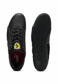 Zapatillas de cuero negro con diseño de cordones, que presentan un acento de logo amarillo y un interior rojo, además de una suela de goma negra texturizada para mayor agarre.