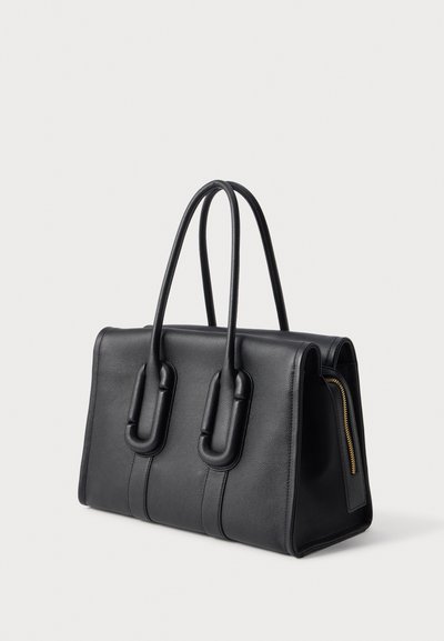 Sac à main en cuir noir avec deux poignées arrondies et une fermeture éclair latérale visible, présenté sur un fond clair uni sous un léger angle.