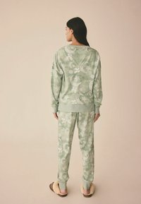 Grønt pyjamassæt består af en afslappet sweatshirt og bukser, begge med et himmelsk mønster af måner og stjerner, lavet af blødt stof.