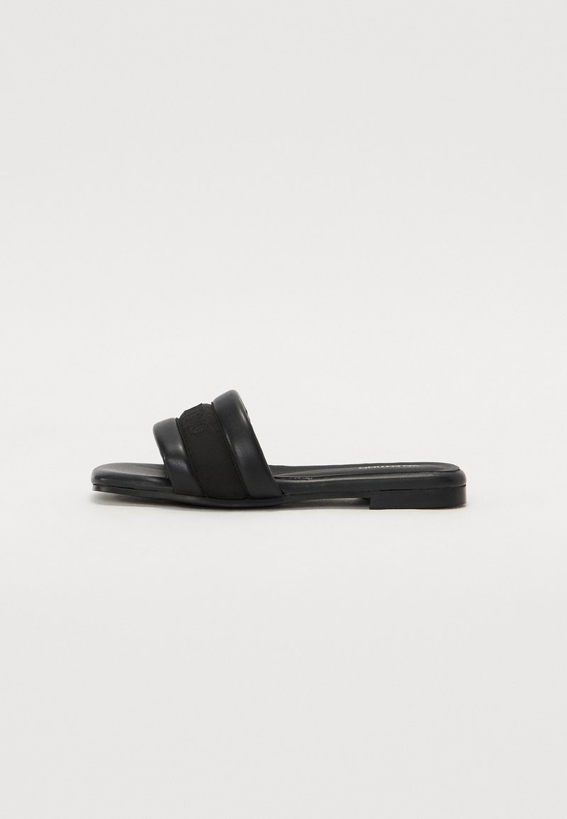 Black slide sandals with two wide straps, one in smooth leather and the other in textured fabric. Flat sole with minimal design.