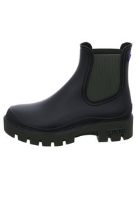 Botín de tobillo negro de goma con un panel elástico verde texturizado, suela gruesa y un acento azul. Cuenta con una etiqueta de la marca en el talón.
