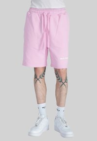Pantalones cortos de algodón rosa con cintura elástica y cordón ajustable, con bolsillos laterales y el texto "MULTIPLY" en blanco en la pierna derecha.