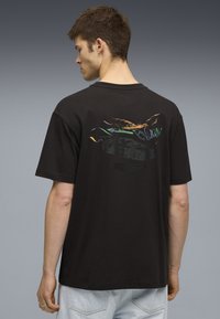 Svart bomullströja med korta ärmar, med en färgglad grafik och textdesign på baksidan. Avslappnad passform och rund hals.