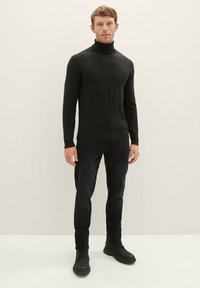 Schwarzer Rollkragenpullover aus weichem Stoff, taillierte Passform mit langen Ärmeln, kombiniert mit dunklen Slim-Fit-Jeans und schwarzen Schnürstiefeln.