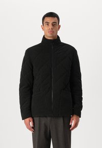 Μαύρο γεμιστό μπουφάν με ψηλό γιακά, μπροστινό φερμουάρ και δύο μεγάλες πλάγιες τσέπες. Κατασκευασμένο από υφασμάτινη ύλη με ζεστή εμφάνιση.