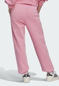 Rosa träningsbyxor med elastisk midja och mudd i nederkant. Slät textur och avslappnad passform, bärs med vita och svarta sneakers.