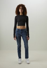Haut court noir à manches longues et ajusté, associé à un jean en denim bleu avec cinq poches et un délavé, complété par des baskets blanches.