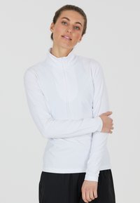 Weißes, langärmeliges Sportoberteil mit hohem Kragen und halbverdecktem Reißverschluss, aus feuchtigkeitstransportierendem Material, enganliegendes Design, glatte Textur.