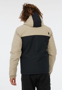 Kapuzenshirt mit einem Farbblockdesign in Beige und Dunkelblau, aus leichtem Stoff gefertigt, mit elastischen Manschetten und Logo der Marke auf dem Rücken.