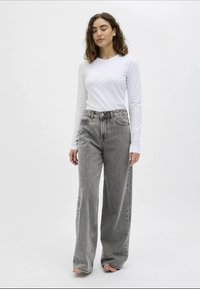 Jeans cinzentos de perna larga com uma cintura alta, costura detalhada e dois bolsos frontais, combinados com uma camisa justa de mangas longas branca.