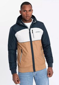 Herren Kapuzenjacke mit Farbblockdesign; marineblau, weiß und tan. Verfügt über Reißverschluss Taschen und elastische Bündchen.