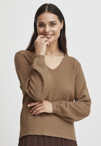 Pull en maille brun avec un col en V, un motif texturé en diamant et des poignets et un ourlet côtelés. La conception présente des manches longues et une coupe décontractée.