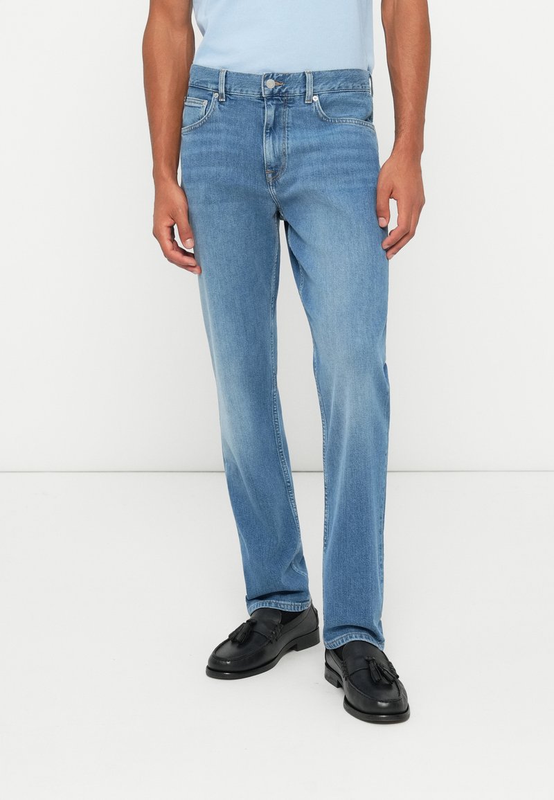 Jeans din denim de culoare albastru deschis, cu croială dreaptă, având un design clasic cu cinci buzunare și închidere cu nasture metalic. Textură netedă și finisaj ușor decolorat.