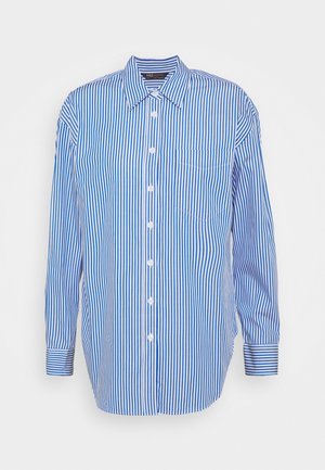Chemise à manches longues rayée verticalement bleu et blanc, boutonnée, avec col et poche poitrine sur fond uni.