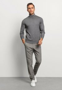 Grau gestrickter Rollkragenpullover aus weichem Material, kombiniert mit hellgrauen, maßgeschneiderten Hosen und weißen Sneakers, die einen stimmigen, lässigen Look schaffen.