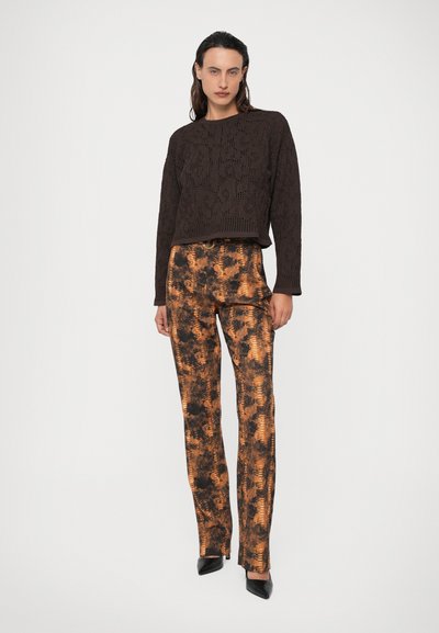 Maglione marrone lavorato a maglia con motivo testurizzato e maniche lunghe, abbinato a pantaloni a vita alta con motivo arancione e nero, e tacchi neri.