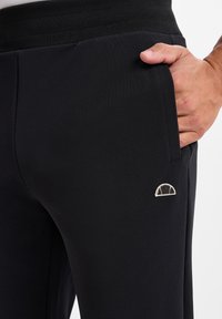 Zwarte sportbroek van textuurstof met een geribbelde tailleband. Heeft een klein geborduurd logo op de linkerkant van de broekzak.